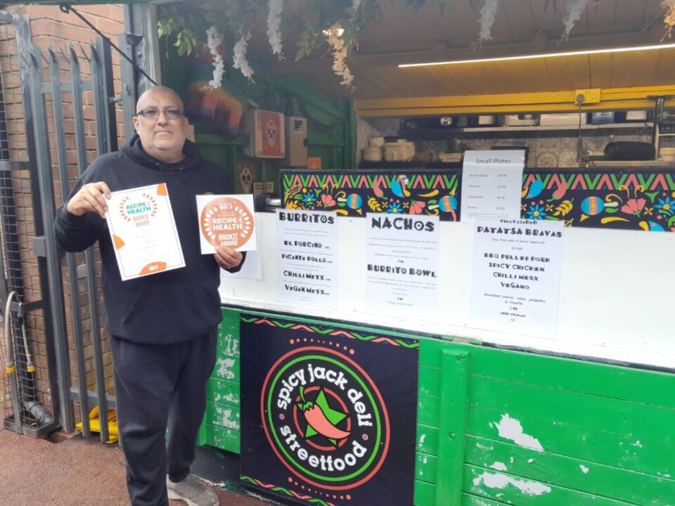 man holding up bronze award certificate in front of his cafe