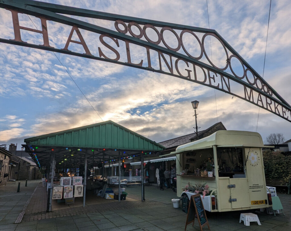 wrought iron sign saying  Haslingden Market with stalls in the background