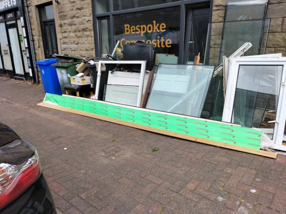 fly tipped rubbish consisting of old doors and windows dumped on pavement outside shop